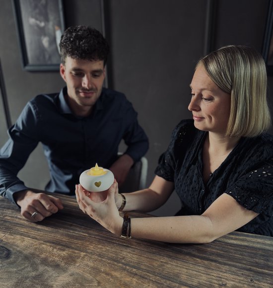 Twee mensen aan tafel met een witte keramieken urn in handen